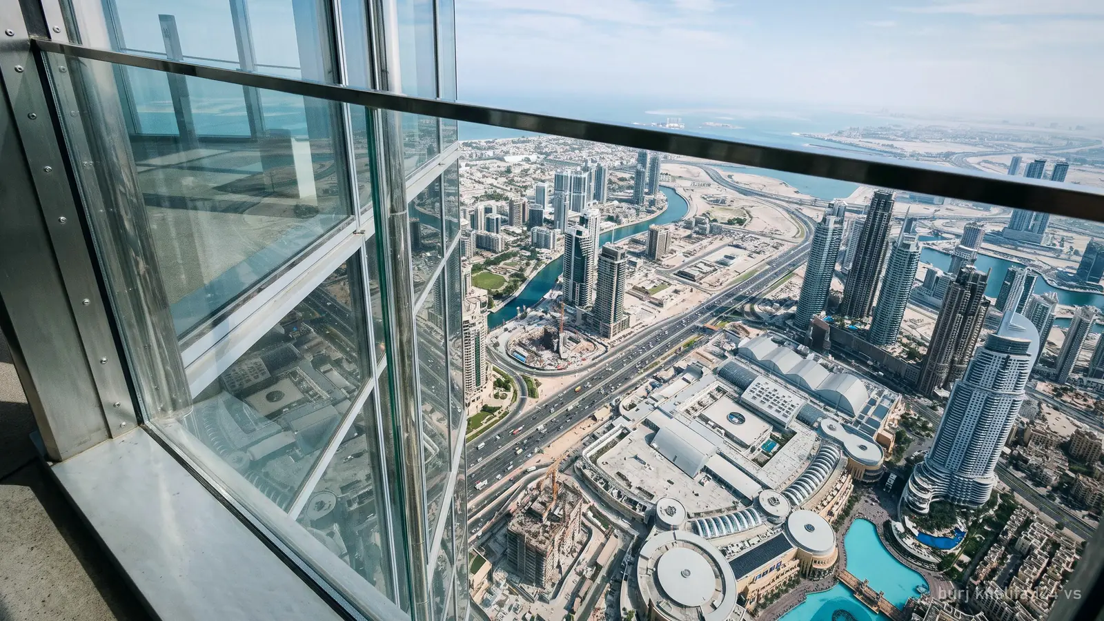 View straight down from a very high skyscraper observation deck window over Downtown Dubai, glass panel edge visible (generated illustration)